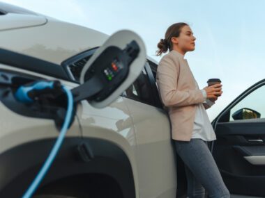 young woman drinking coffee standing next to an EV charging