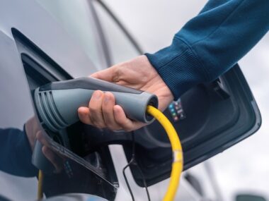 Man plugging in charger into an electric car at charge station